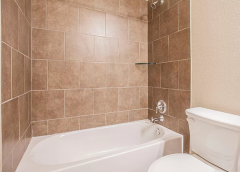 A white bathtub sits next to a toilet in a bathroom with brown tiled walls.