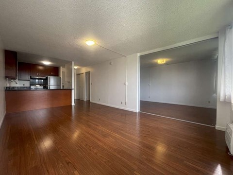 A room with wooden floors and a kitchen area to the left.