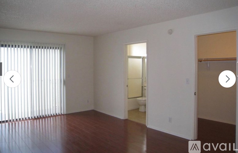 A room with wooden floors and white walls, with a door leading to a bathroom.