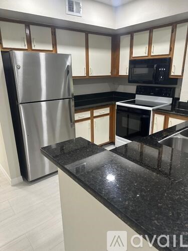 A kitchen with a black countertop and a stainless steel refrigerator.
