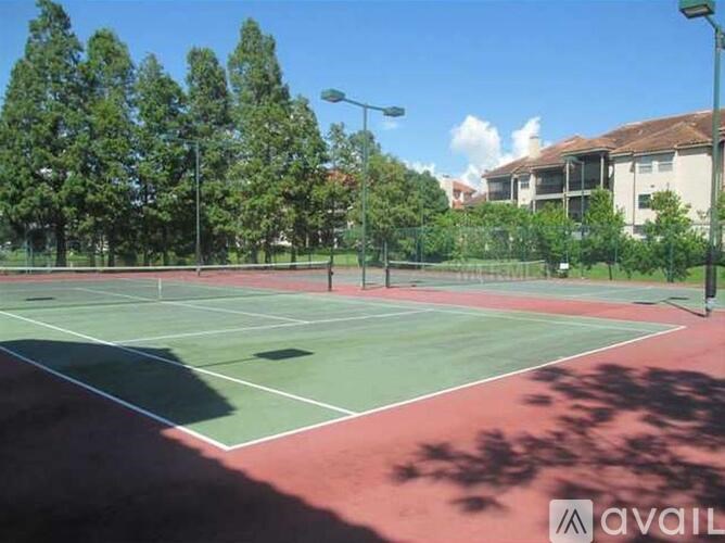A tennis court with a green and red surface surrounded by trees and buildings.