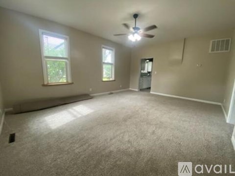 A spacious room with a ceiling fan and two windows.