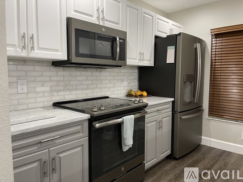 A kitchen with a black refrigerator, white cabinets, and a black stove top.