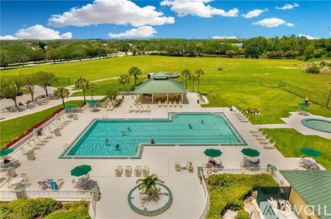 A large outdoor swimming pool surrounded by a grassy area and a pavilion.