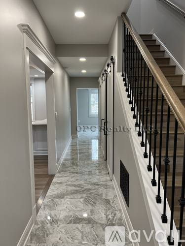 A long hallway with a marble floor and a staircase with black railings.