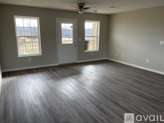 A spacious room with a ceiling fan and two windows.