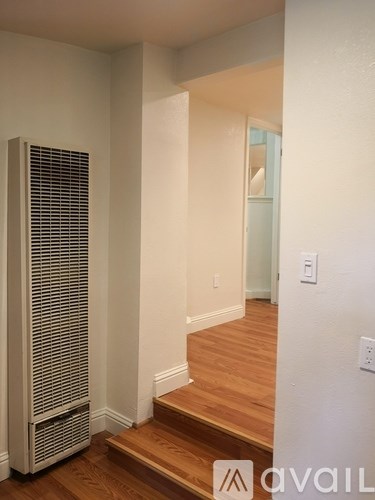 A tall white air conditioning unit sits on a wooden floor next to a staircase.