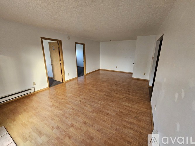 A room with wooden flooring and white walls, with a door on the left and a window on the right.