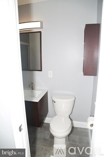 A white toilet in a small bathroom with a white sink and a mirror.