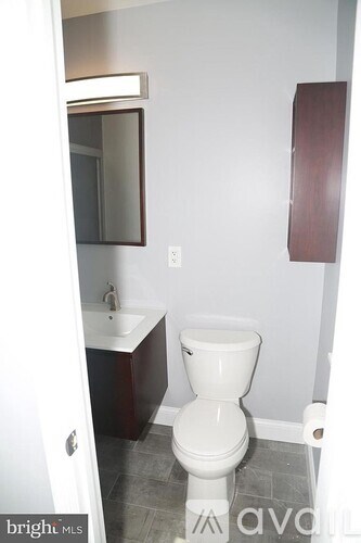 A white toilet in a small bathroom with a white sink and a mirror.