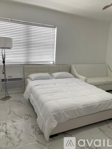 A white bed with a white bedspread is in a room with a marble floor.