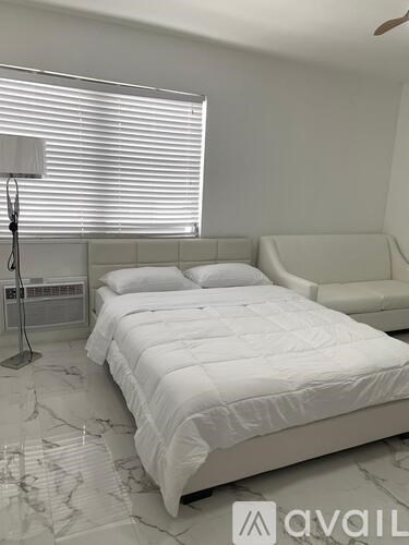 A white bed with a white bedspread is in a room with a marble floor.