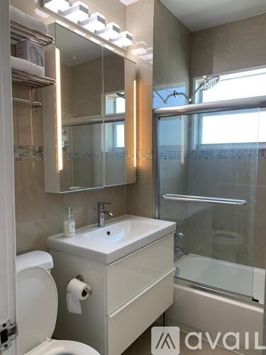 A bathroom with a sink, toilet, mirror, and shower.