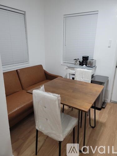 A brown couch sits in a living room with a wooden table and white chairs.