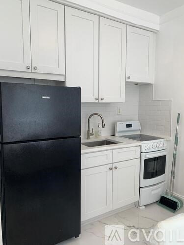 A black refrigerator is in a kitchen with white cabinets.