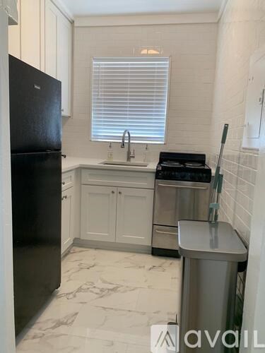 A kitchen with a black fridge, white cabinets, and a marble floor.