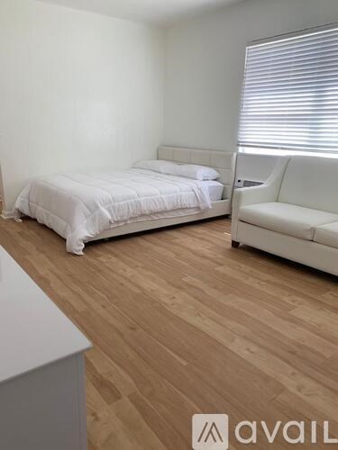 A bedroom with a bed, a couch, and a wooden floor.