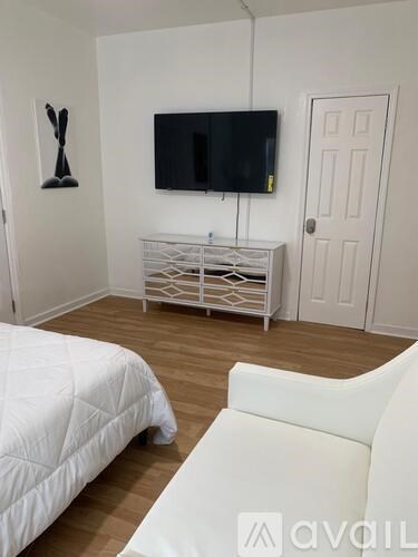 A white bedroom with a bed, a TV, and a cabinet.