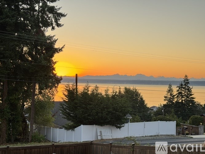 A sunset view with a white fence and trees in the foreground.