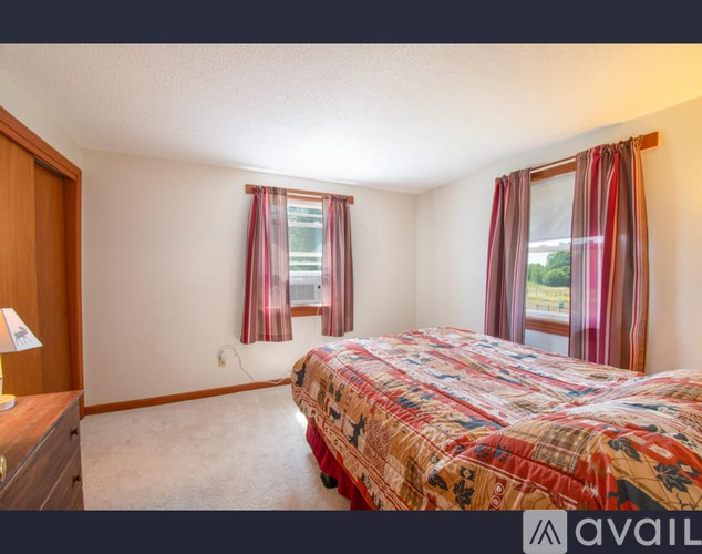 A bedroom with a bed, nightstand, and window with curtains.