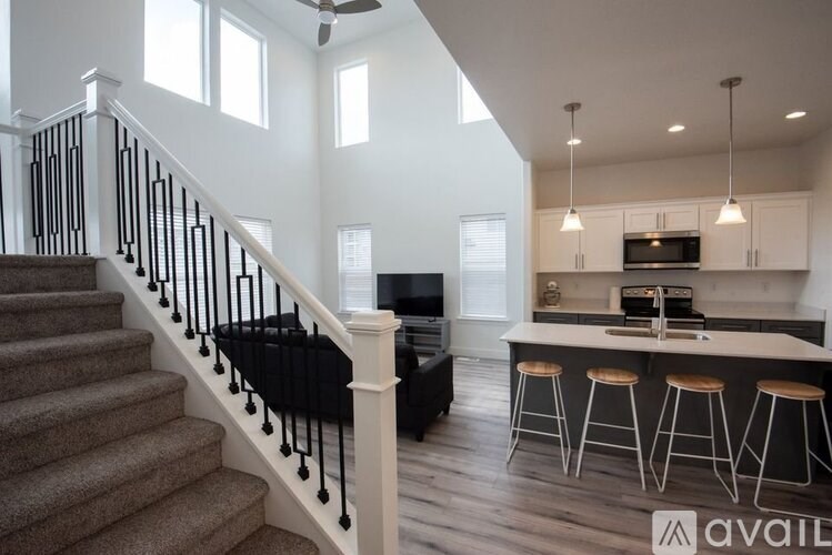 A staircase with a black railing and a white balustrade leads to a living room with a bar and stools.