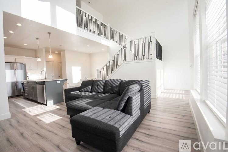 A modern living room with a black sofa and a kitchen area in the background.