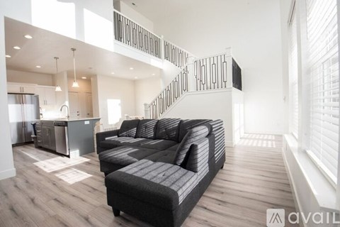 A modern living room with a black sofa and a kitchen area in the background.