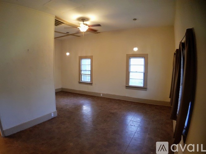 A room with brown flooring and two windows.