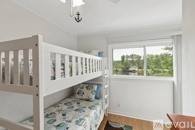 A white bunk bed with a blue and white bedspread in a room with a window.