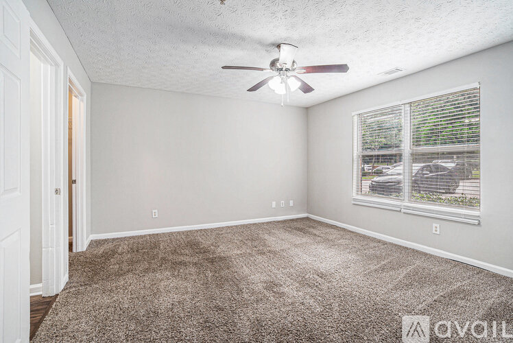 A room with a carpeted floor, a ceiling fan, and a window with blinds.