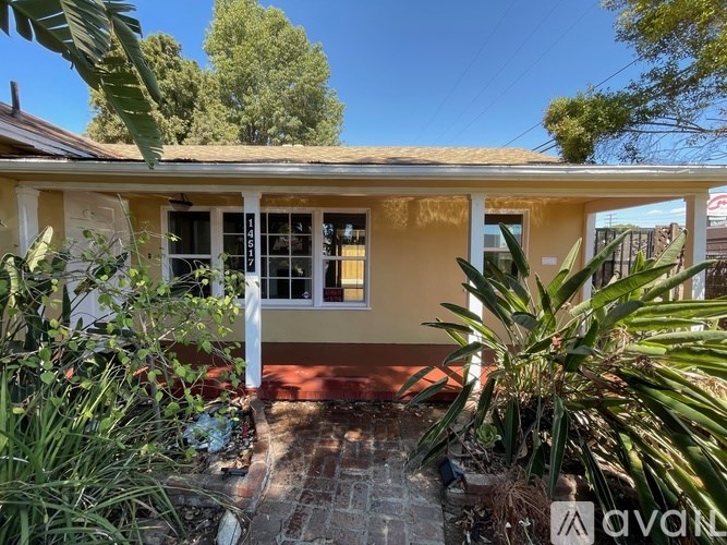 A yellow house with a red door and windows surrounded by green plants.