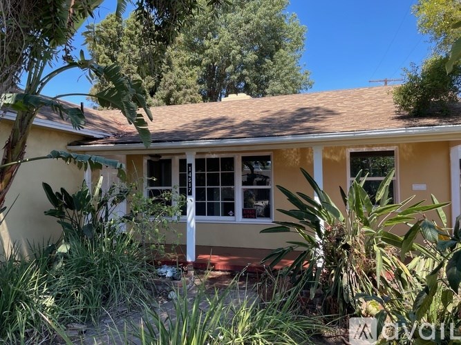 A house with a brown roof and a white door surrounded by green plants.