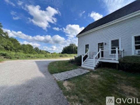 A white house with a porch and a gravel driveway.
