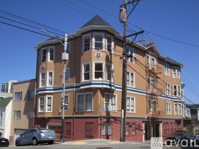 A large brown building with a green roof is in the foreground with cars parked in front.