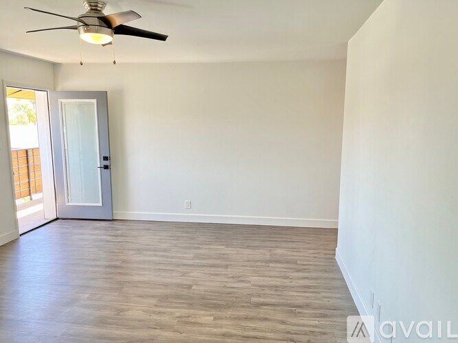A room with a ceiling fan and light fixture, wooden flooring, and a door leading to a balcony.