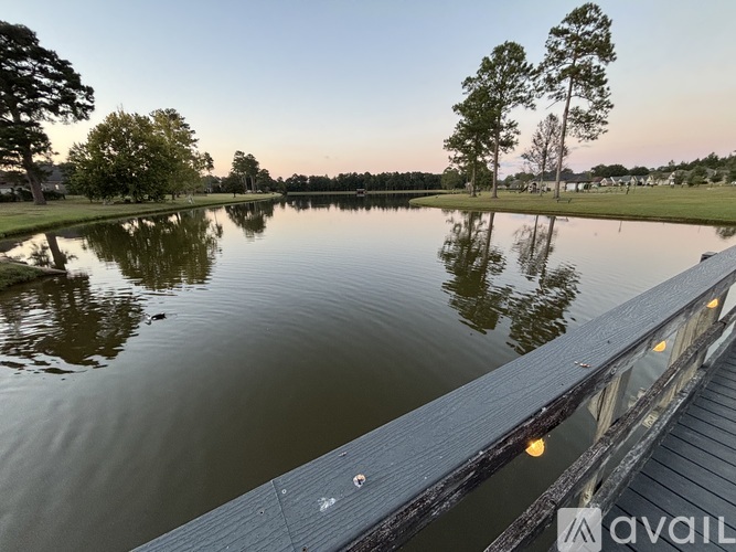 A serene lake with a wooden dock and trees in the background during sunset.