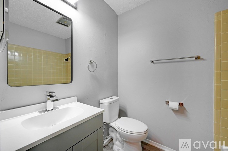 A bathroom with a toilet, sink, mirror, and towel rack.