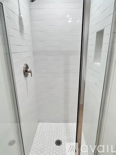 A white tiled shower with a silver faucet.