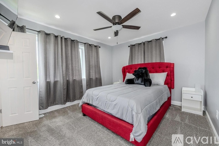 A bedroom with a red headboard bed, a ceiling fan, and a window with curtains.