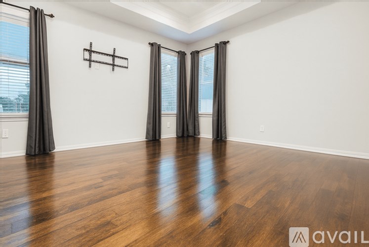 A room with wooden floors and two windows with black curtains.