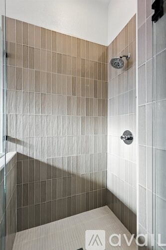 A shower area with a glass door and brown tiles.