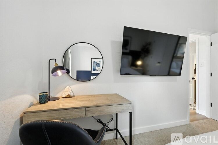 A black chair sits in front of a desk with a round mirror above it.