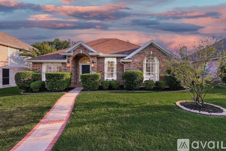 A house with a brick facade and a white door is surrounded by a well-manicured lawn.