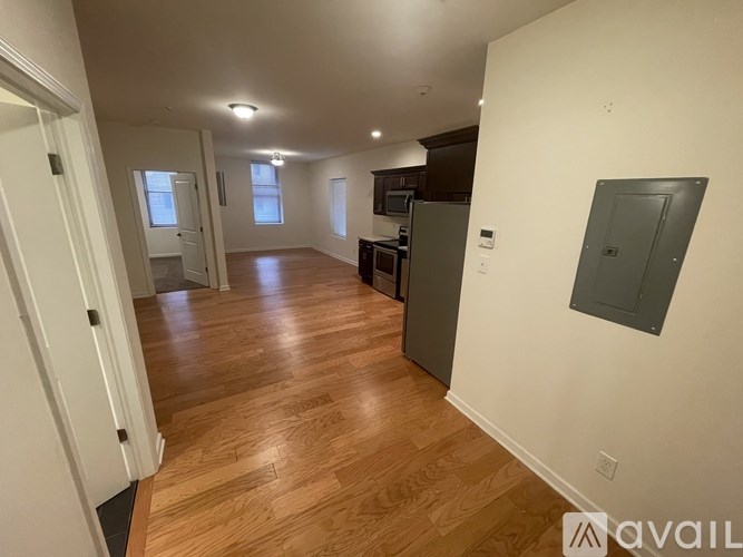 A spacious room with wooden flooring and a kitchen area with a refrigerator, microwave, and oven.