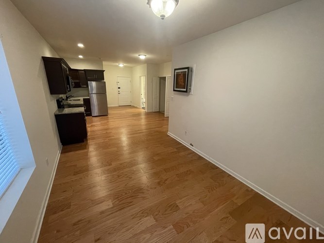 A long hallway with wooden floors and a kitchen area in the background.