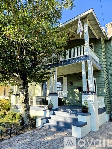 A green house with a white porch and a tree in front.