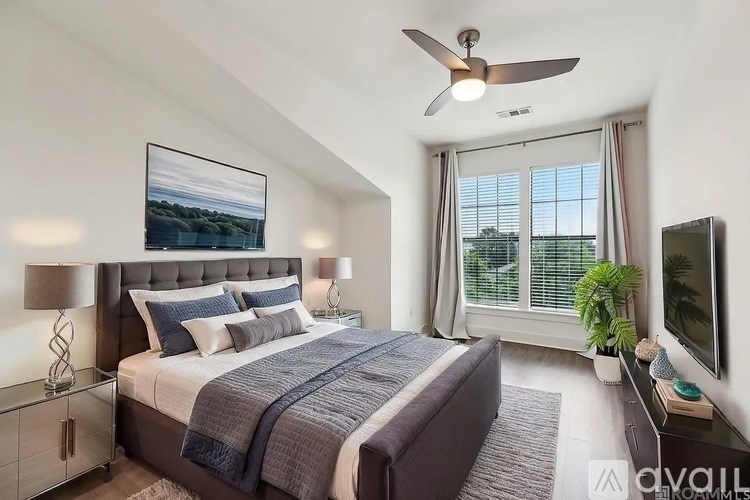 A bedroom with a large bed, a ceiling fan, and a painting on the wall.