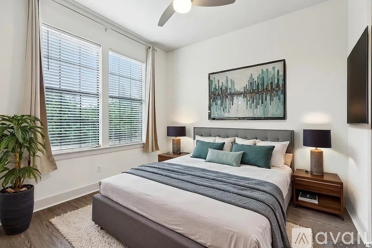 A bedroom with a large bed, a potted plant, and a painting on the wall.