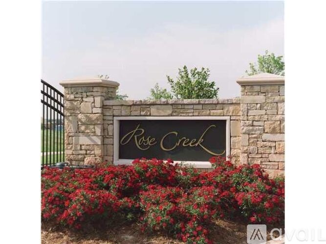 A sign that says Rose Creek is surrounded by red flowers.