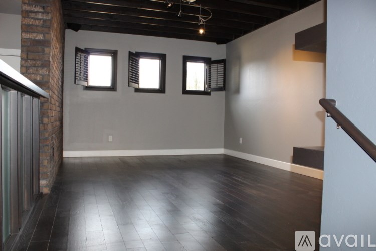 A room with dark wood flooring and three windows with blinds.